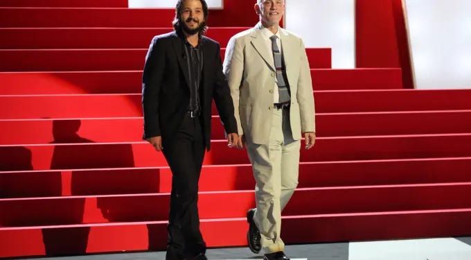 Diego Luna in black suit and John Malkovich in beige suit on stage