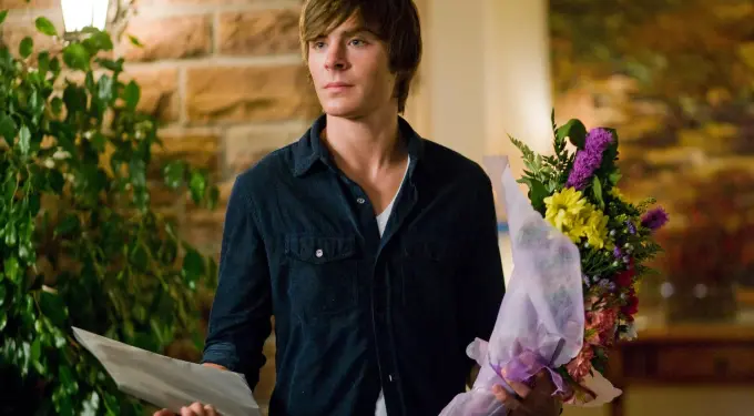 young man stands holding flowers wrapped in paper and a letter