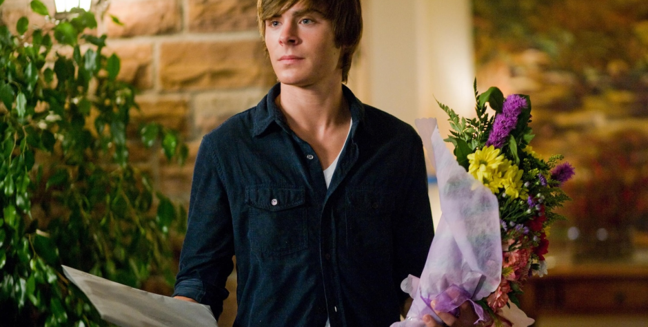 young man stands holding flowers wrapped in paper and a letter