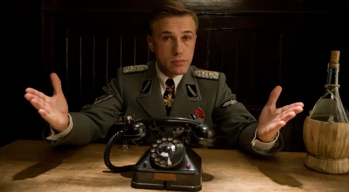 Christoph Waltz as Nazi officer gesturing at table with old phone