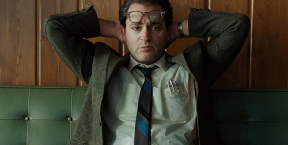 Michael Stuhlbarg in suit with glasses sitting back with arms behind head
