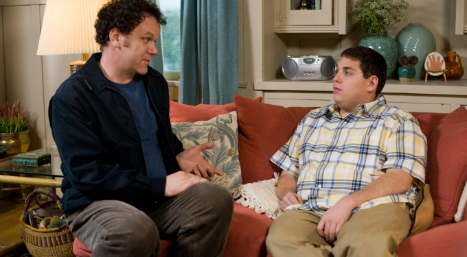 Two men seated on couch engaged in serious conversation indoors