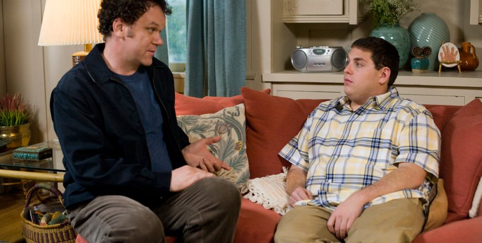 Two men sitting on couch, one gesturing, talking in living room