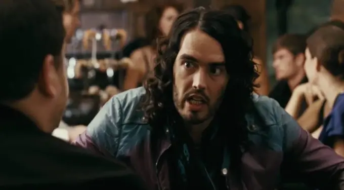 man with long curly hair talks intensely in a crowded bar