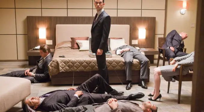 man in suit stands in hotel room with several unconscious men