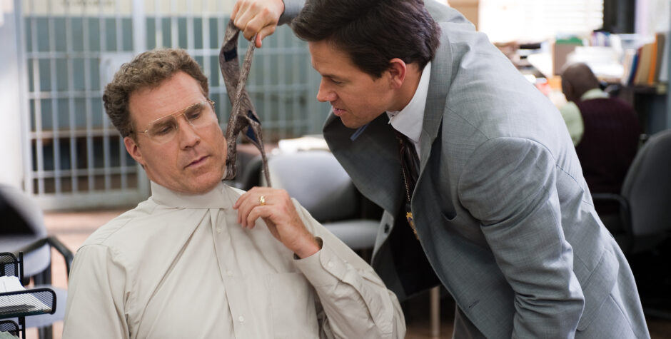 Mark Wahlberg leans toward seated Will Ferrell holding a tie