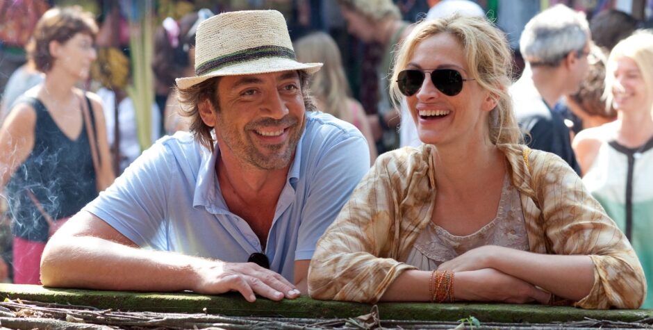 Man in straw hat and woman in sunglasses laugh leaning on outdoor railing