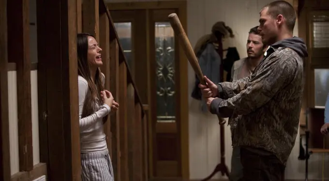 Woman distressed against wall, man holds baseball bat confronting her inside house