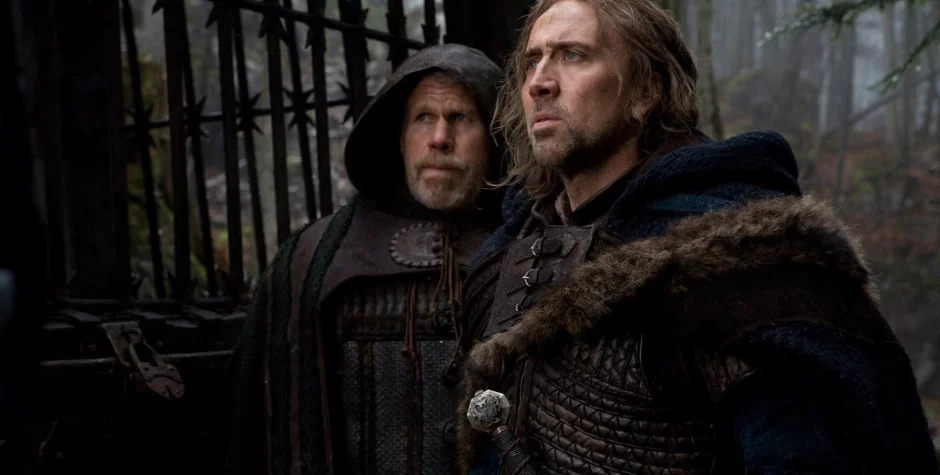 Ron Perlman and Nicolas Cage in medieval costumes near gate