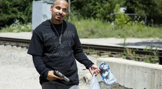Michael Peña holding a gun and two trash bags by railroad tracks