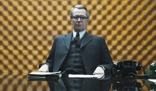 Man in suit and glasses sits behind desk with old phones