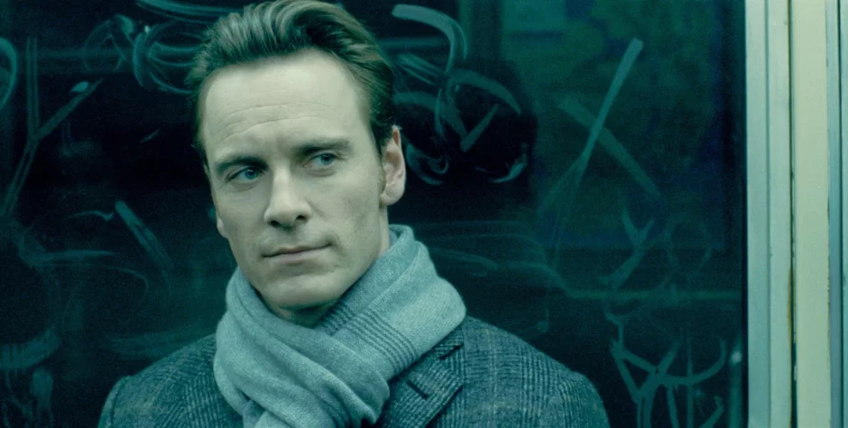 Michael Fassbender in coat and scarf by graffiti-covered window