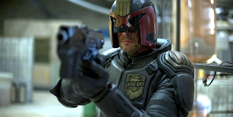 Karl Urban as Judge Dredd aiming gun in armored suit and helmet