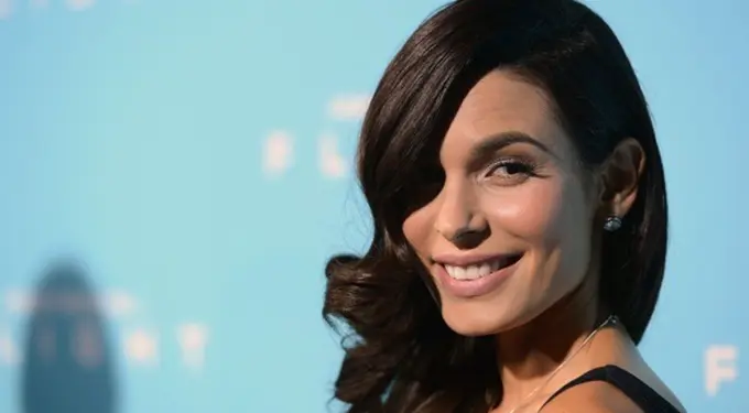 Nadine Velazquez smiling in black dress at blue background