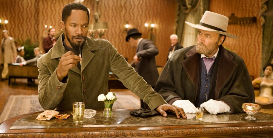 Jamie Foxx and Franco Nero sit at bar table in period western scene