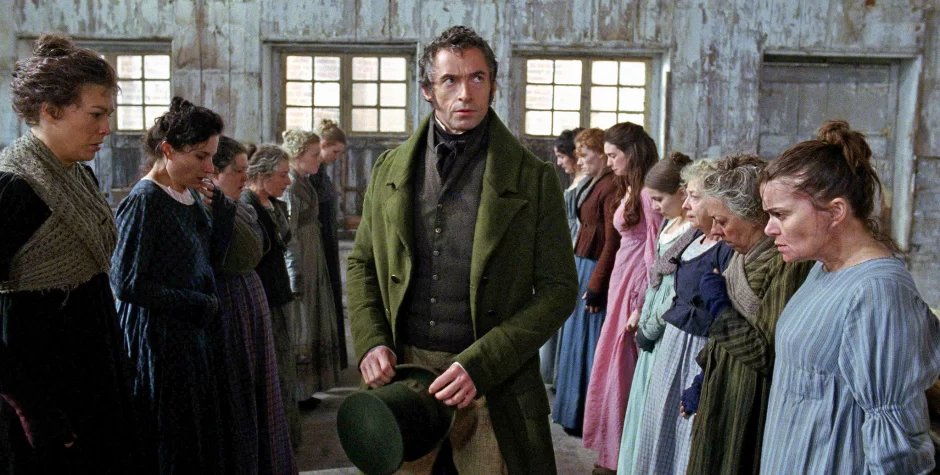 Hugh Jackman in green coat among lined-up women in period clothing