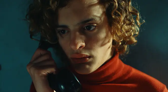young man with curly hair holds black phone receiver looking serious