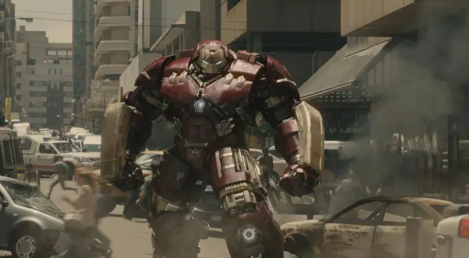 Hulkbuster armor in battle stance on a city street with smoke and damaged cars