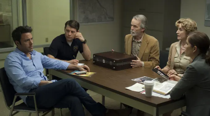 Five people in a tense meeting around a table with briefcase