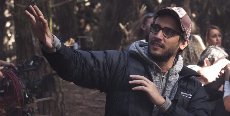 Director Fede Alvarez gestures with hand, wearing glasses and cap outdoors