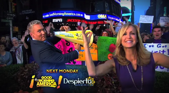 two morning show hosts pose with crowd and signs behind them