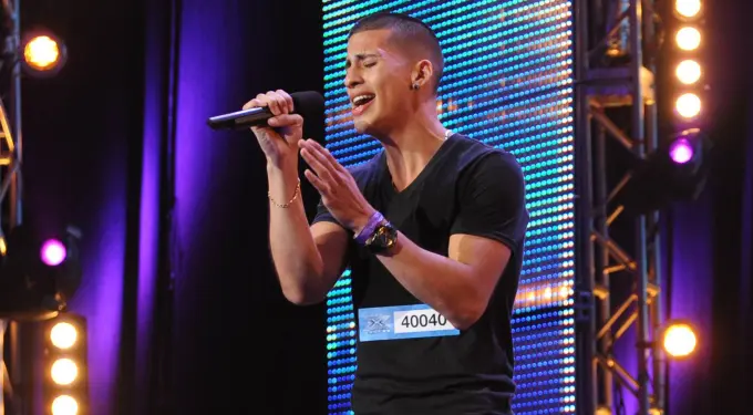 Carlito Olivero singing during a stage audition with blue lights