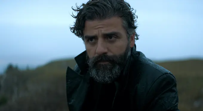 Oscar Isaac with beard and dark coat in serious movie scene outdoors