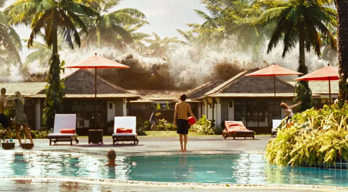 People by pool with palm trees as giant wave crashes behind