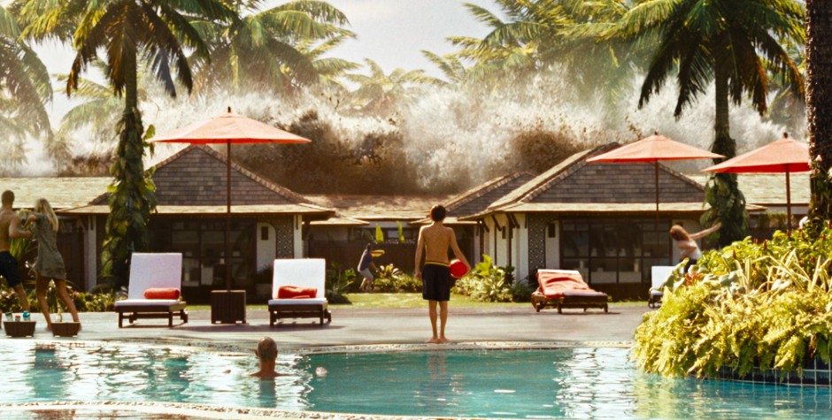 People by pool with palm trees as giant wave crashes behind