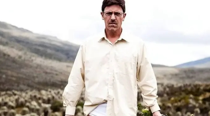 Man in white shirt holding gun in barren outdoor landscape