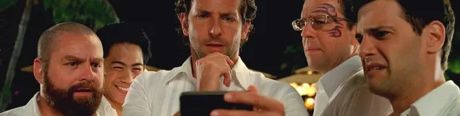 five men stare at cellphone screen outdoors at night