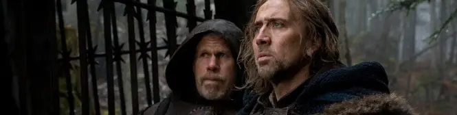 two men in medieval clothes near iron fence in forest setting