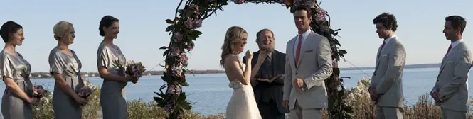 Bride and groom exchange vows under floral arch by water