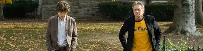 Two men walking outside on autumn leaves near tree and stone wall