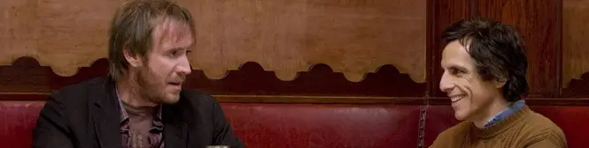 Two men talk in a restaurant booth with red seats and wood paneling