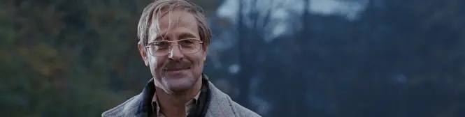 man with glasses and mustache smiling outdoors in jacket