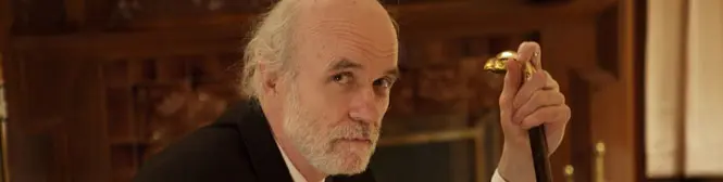 older man with beard holding cane in dark suit indoors
