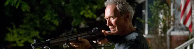 Man aims rifle outside a house at night, focused expression