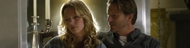 man and woman sit close indoors in serious movie scene