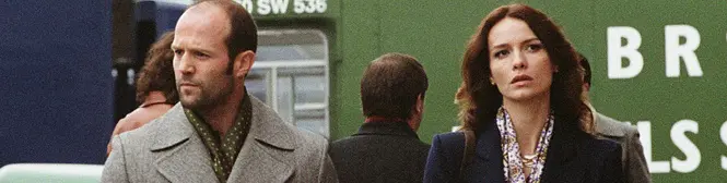Man and woman walk past green sign outside in coat and blazer