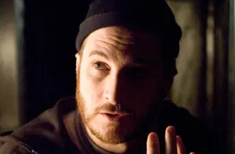 man in dark hat and jacket looking sideways in low light
