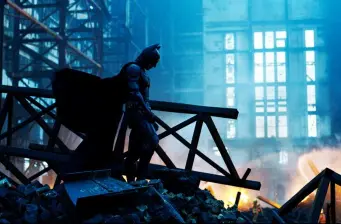 Batman stands on rubble inside a steel-framed building at night