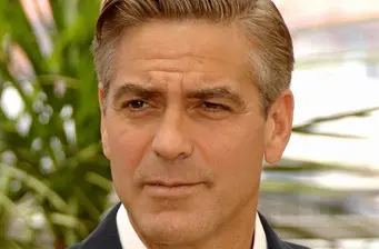 Close-up headshot of George Clooney outdoors with plants behind him