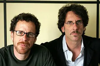 Two men, likely filmmakers, sitting side by side against plain wall