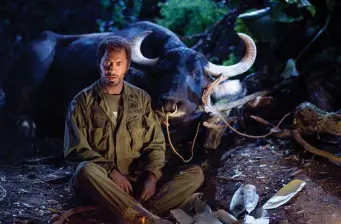 Man in army clothes sitting near buffalo in dark forest scene
