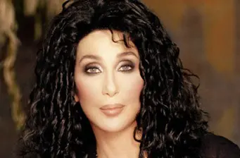 Close-up headshot of Cher with dark curly hair and makeup