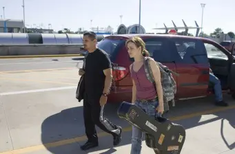 man and woman walk with bags near red van on tarmac