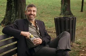 Man in blazer sitting on park bench holding water bottle