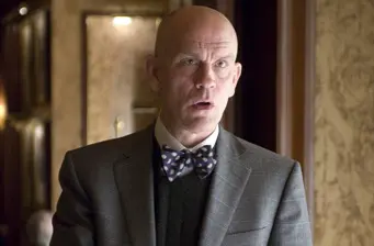 Man in gray suit and polka dot bow tie in dim room