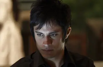 man with dark hair looks down in low light scene